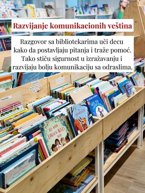 Drvene police u obliku kutija pune su šarenih slikovnica okrenutih koricama ka posetiocima, a u pozadini stoji žena.