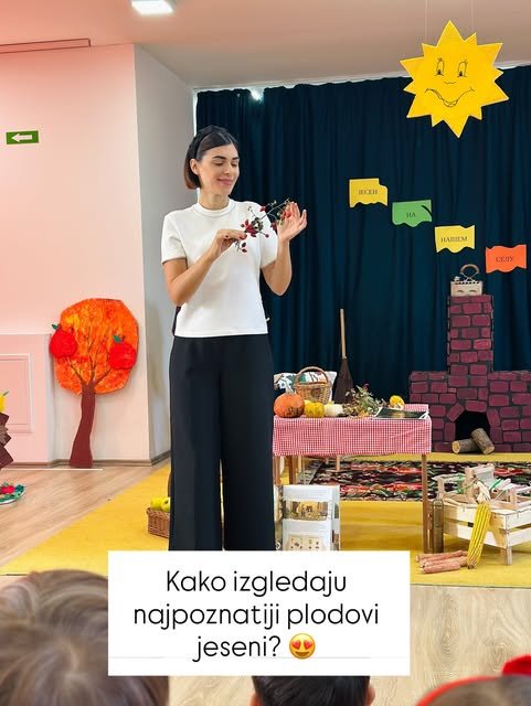 Nevena Jovičić deci pokazuje grančicu sa crvenim plodovima, a iza nje je sto sa bundevama i korpom.