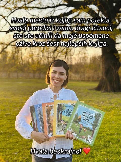 Nasmejana autorka u beloj bluzi drži u rukama šest slikovnica ispred starog drveta u jesenjem svetlu.
