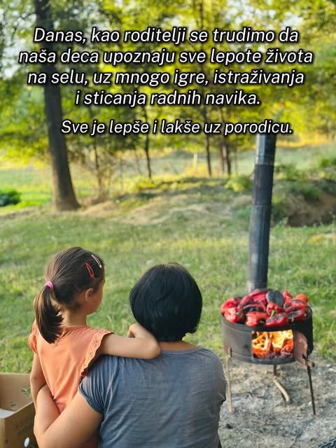Majka drži devojčicu u naručju dok zajedno gledaju crvene paprike koje se peku na vatri u dvorištu.
