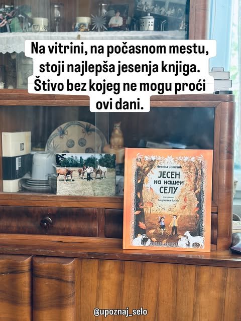 Slikovnica Jesen na našem selu stoji na drvenoj vitrini pored porodične fotografije konja i starog posuđa.