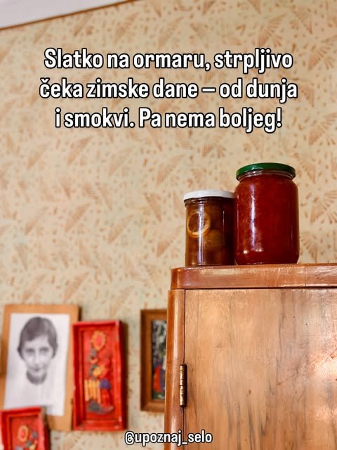 Dve tegle domaćeg slatka od dunja i smokava stoje na vrhu drvenog ormara ispred zida sa uramljenim slikama.