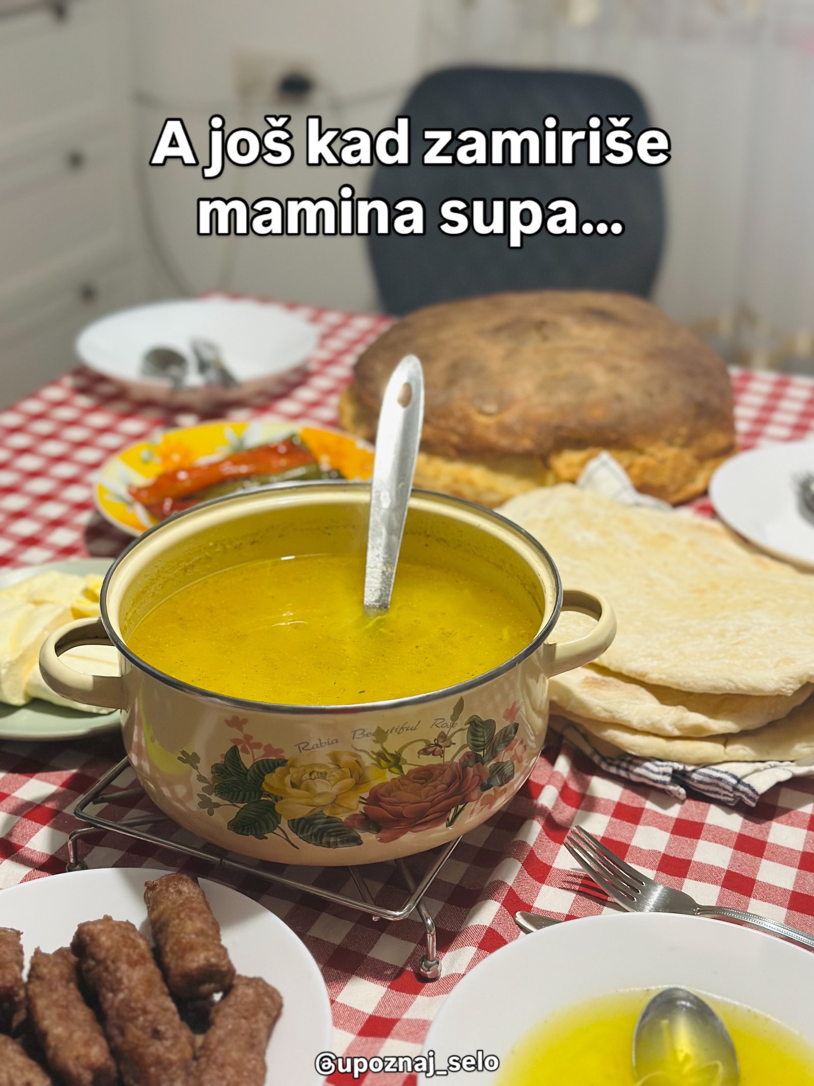 Šerpa supe sa šarom ruža na crveno-belom stolnjaku, pored okruglog hleba, ćevapa i pečenih paprika.