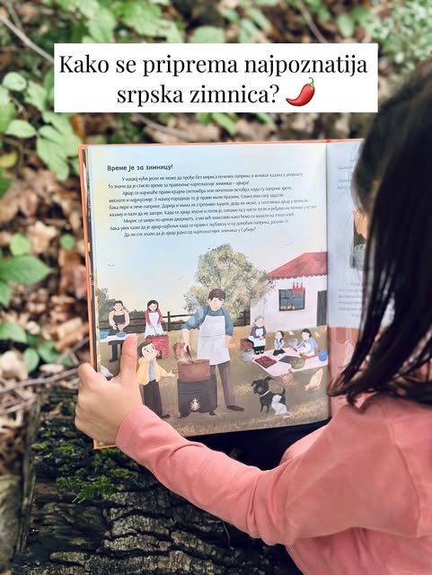 Devojčica u roze džemperu drži knjigu otvorenu na stranici o zimnici, gde porodica sprema ajvar u dvorištu.