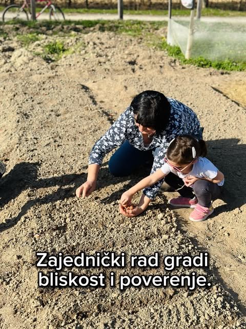 Žena i devojčica sa naočarima čuče nad zemljom i zajedno stavljaju seme u leju.
