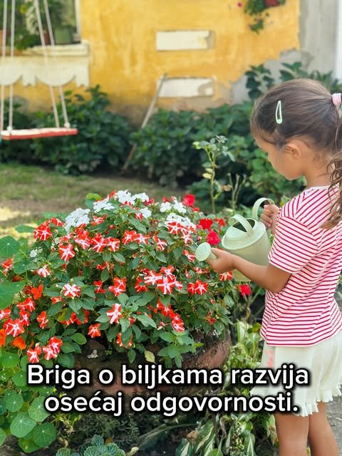 Devojčica sa crvenim prugama zaliva žbun cveća zelenom kanticom pred žutom kućom i ljuljaškom.