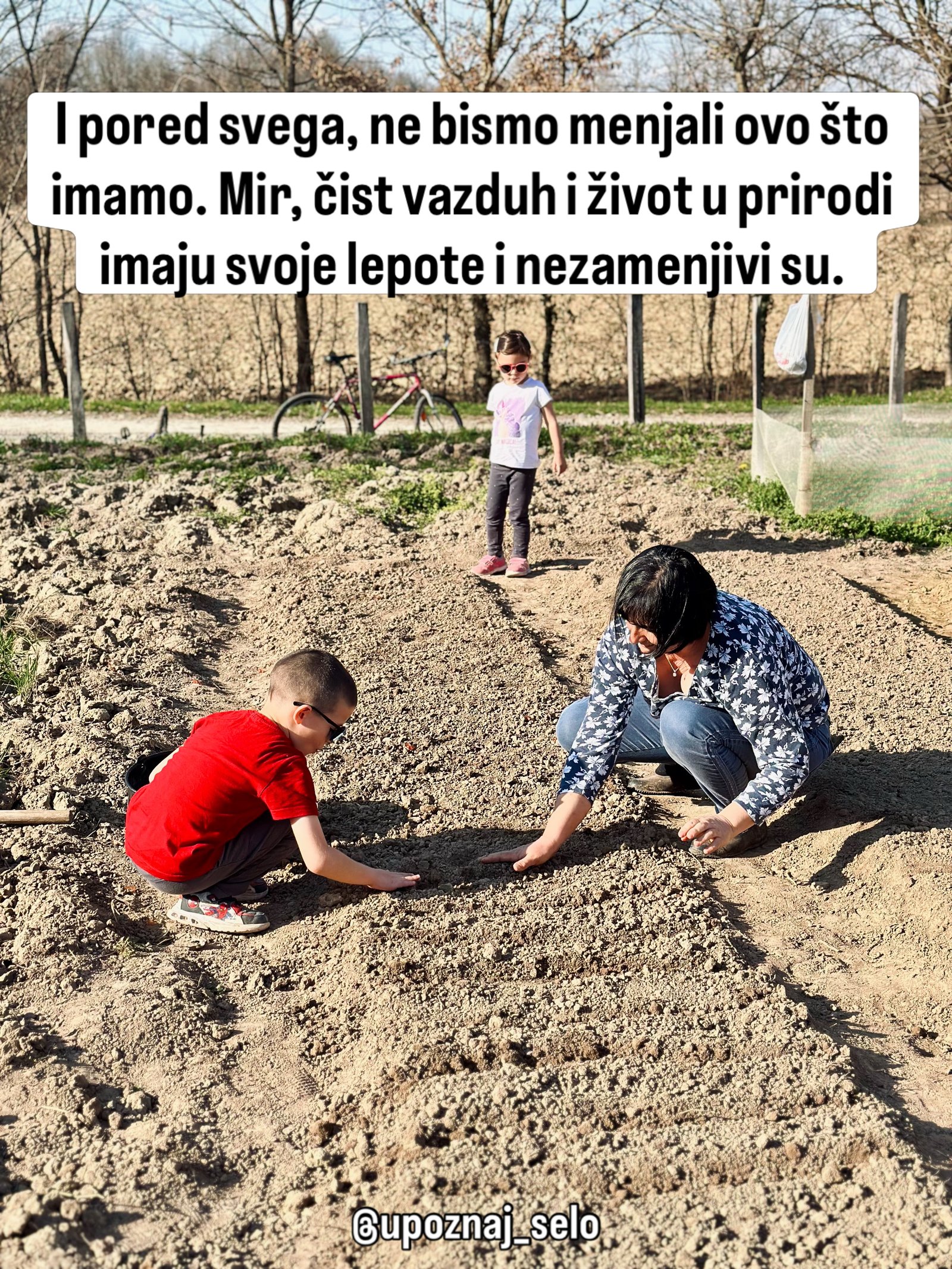 Žena i dečak u crvenoj majici čuče nad lejom, a devojčica u naočarima stoji iza njih.
