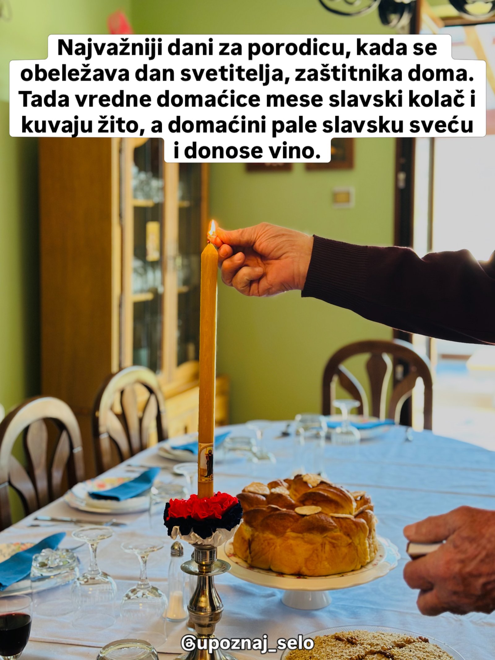 Ruka pali visoku žutu sveću ukrašenu trobojkom, a pored nje na postolju stoji slavski kolač.