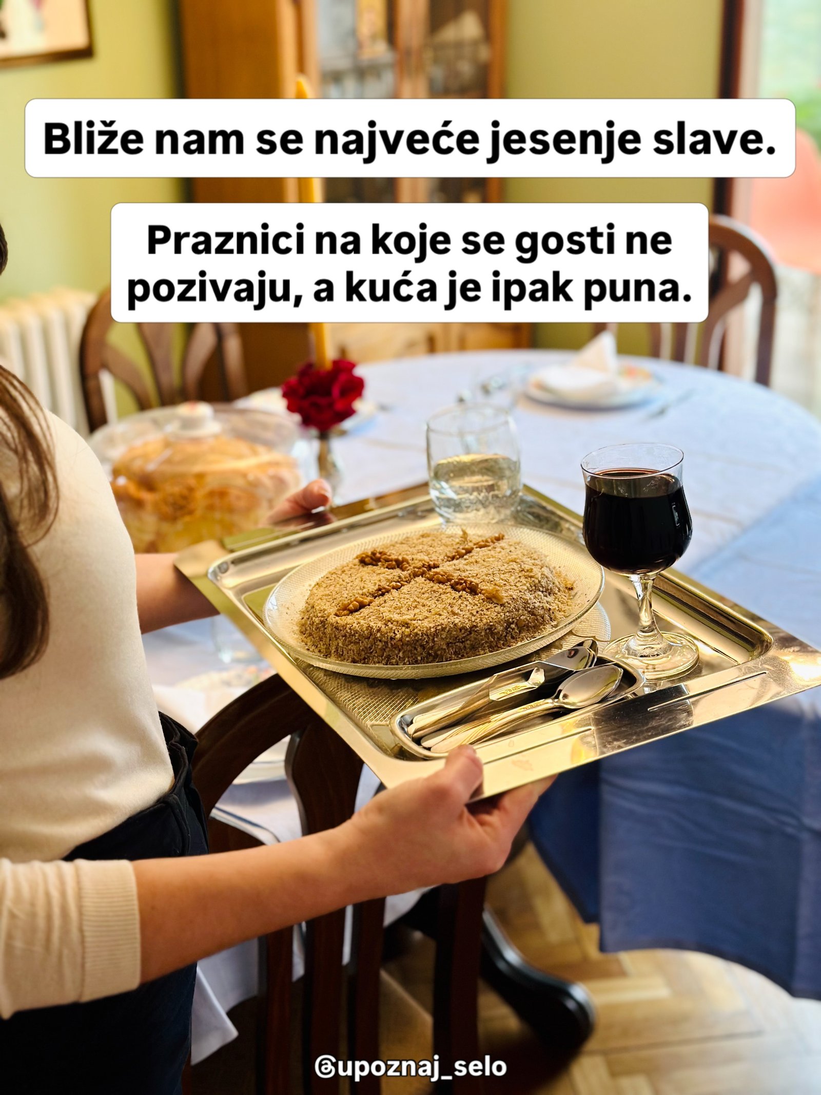 Žena nosi srebrni poslužavnik sa ukrašenim žitom, čašom crnog vina i kašičicama ka postavljenom stolu.