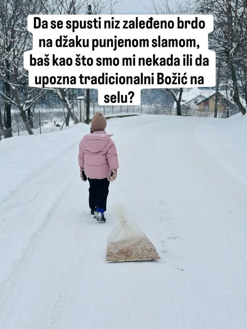 Dete u roze jakni vuče providnu vreću napunjenu slamom po belom, snegom prekrivenom seoskom putu.